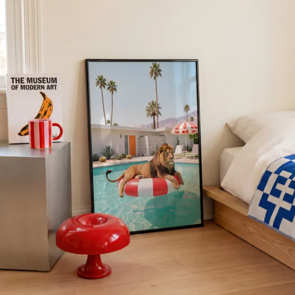 Black framed Lion at Leisure art print styled beside a modern bed with red accents