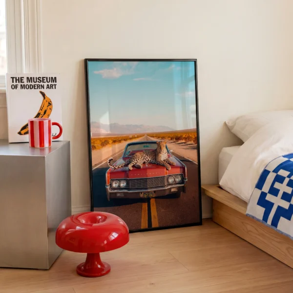 Black framed leopard desert highway wall art styled beside a modern bed with bold red accents