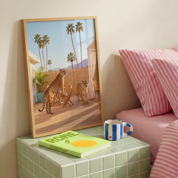 Two tigers patio framed print beside pink striped bedding on a tiled bedroom table