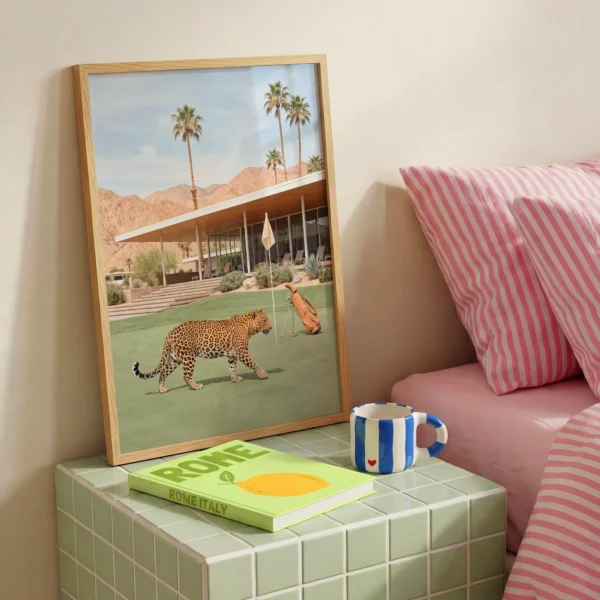 Framed leopard golf course print on a bedroom side table beside pink striped bedding