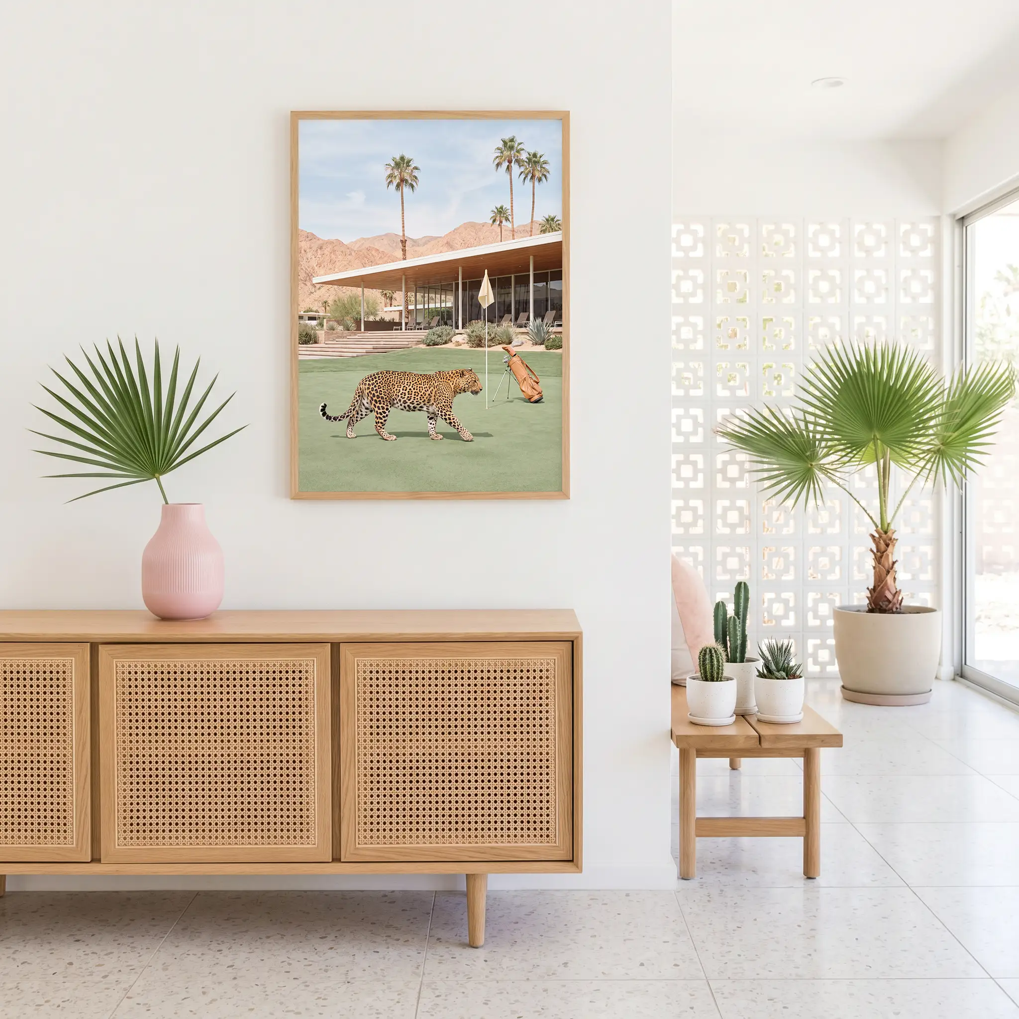 Leopard golf art in a natural wood frame above a cane-front sideboard, with a pink vase and indoor palms